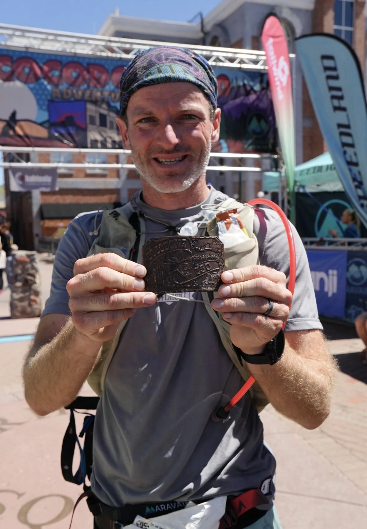 Josh Frewin holding his Cocodona 250 finisher buckle at the finish line