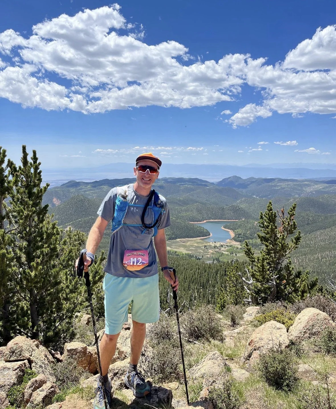Josh Frewin on a mountain summit above a lake wearing race bib 112