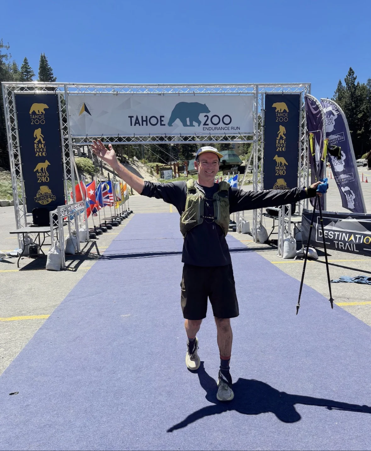 Josh Frewin crossing the Tahoe 200 finish line with trekking poles and arms outstretched
